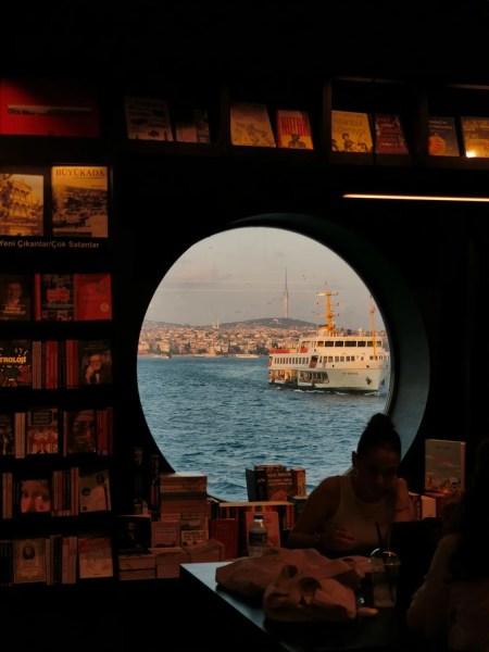 Photo of a round window toward the sea from the interior of a cozy bookstore