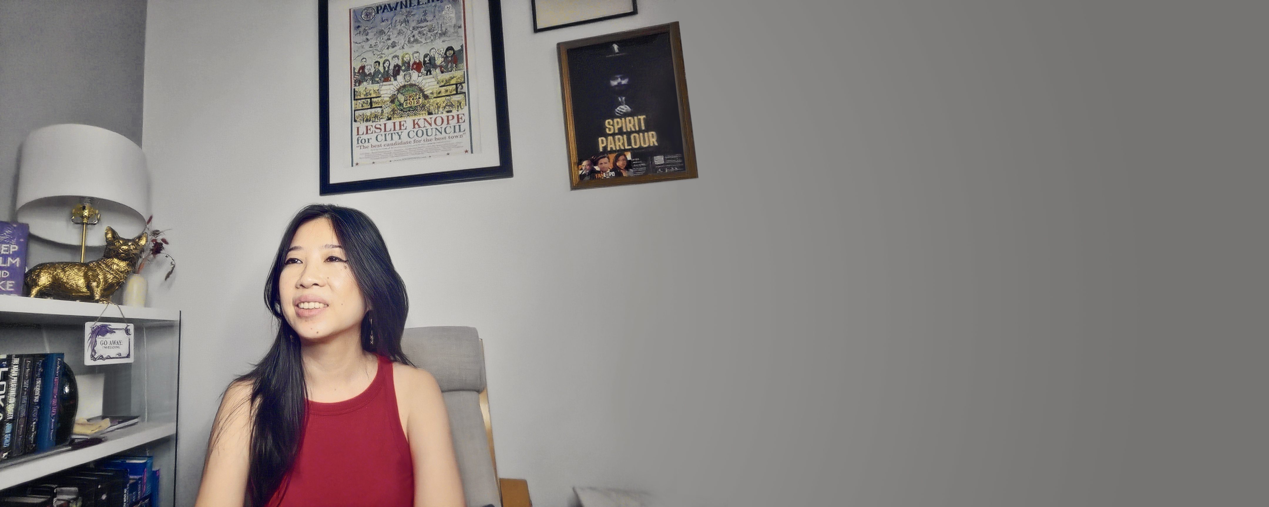 Photo of the author smiling in front of a bookshelf and wall art